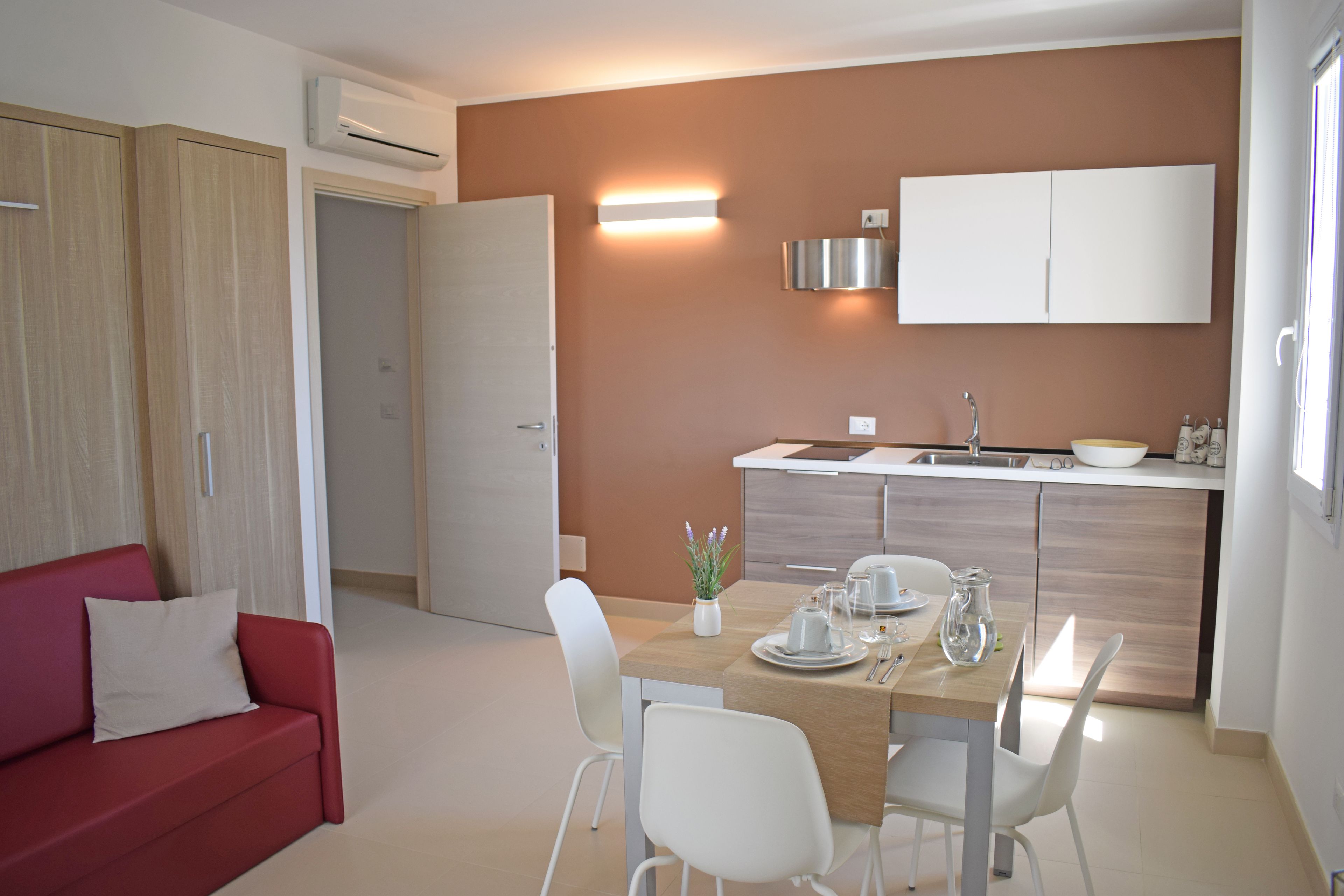 Una cocina moderna con horno empotrado, un comedor con mesa para dos y un sofá rojo en la sala.