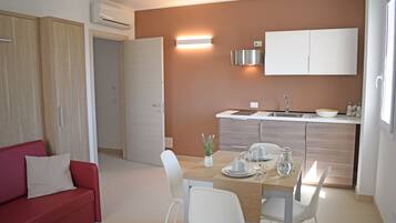Una cocina moderna con horno empotrado, un comedor con mesa para dos y un sofá rojo en la sala.