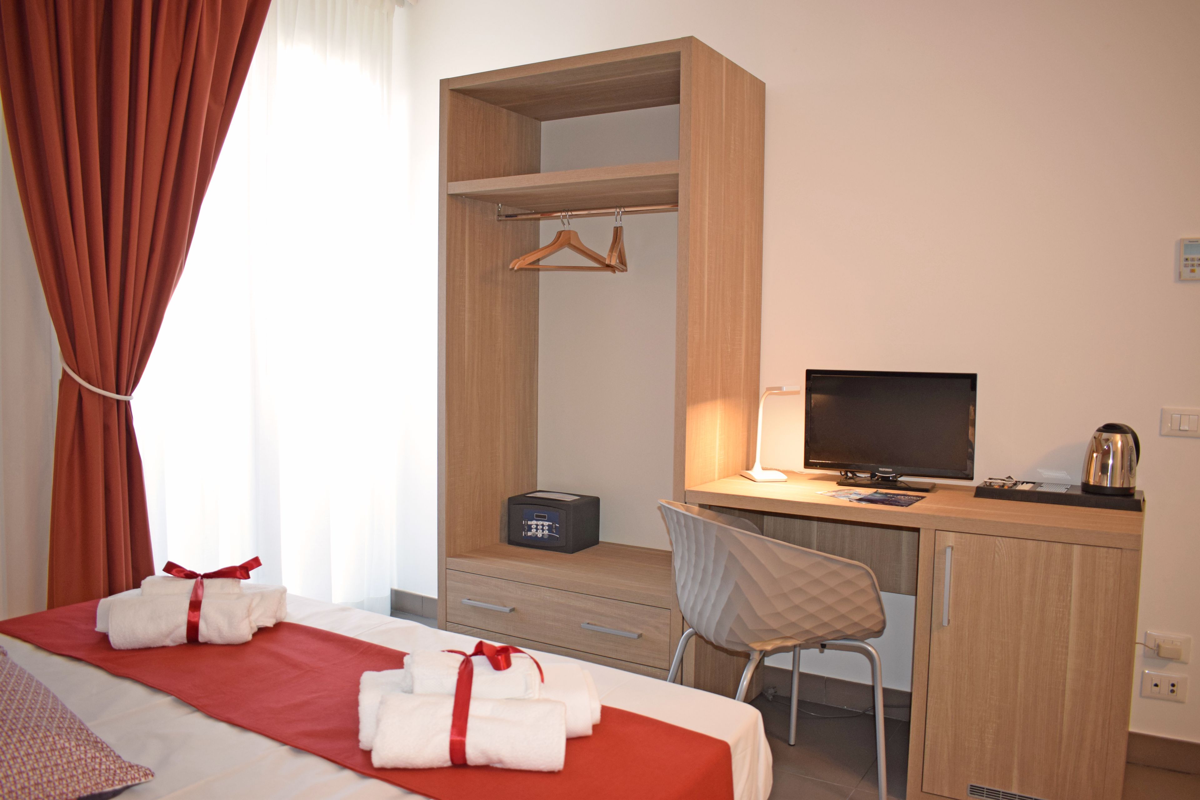 A hotel room with a bed, a desk, a chair, a TV, and a wardrobe.