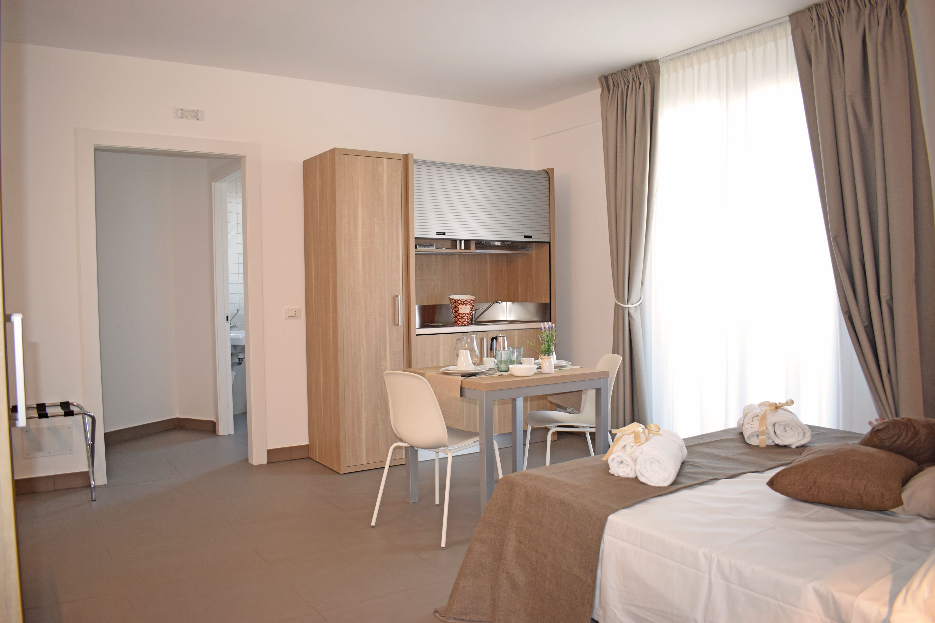 A modern hotel room with a bed, a desk, and a kitchenette.