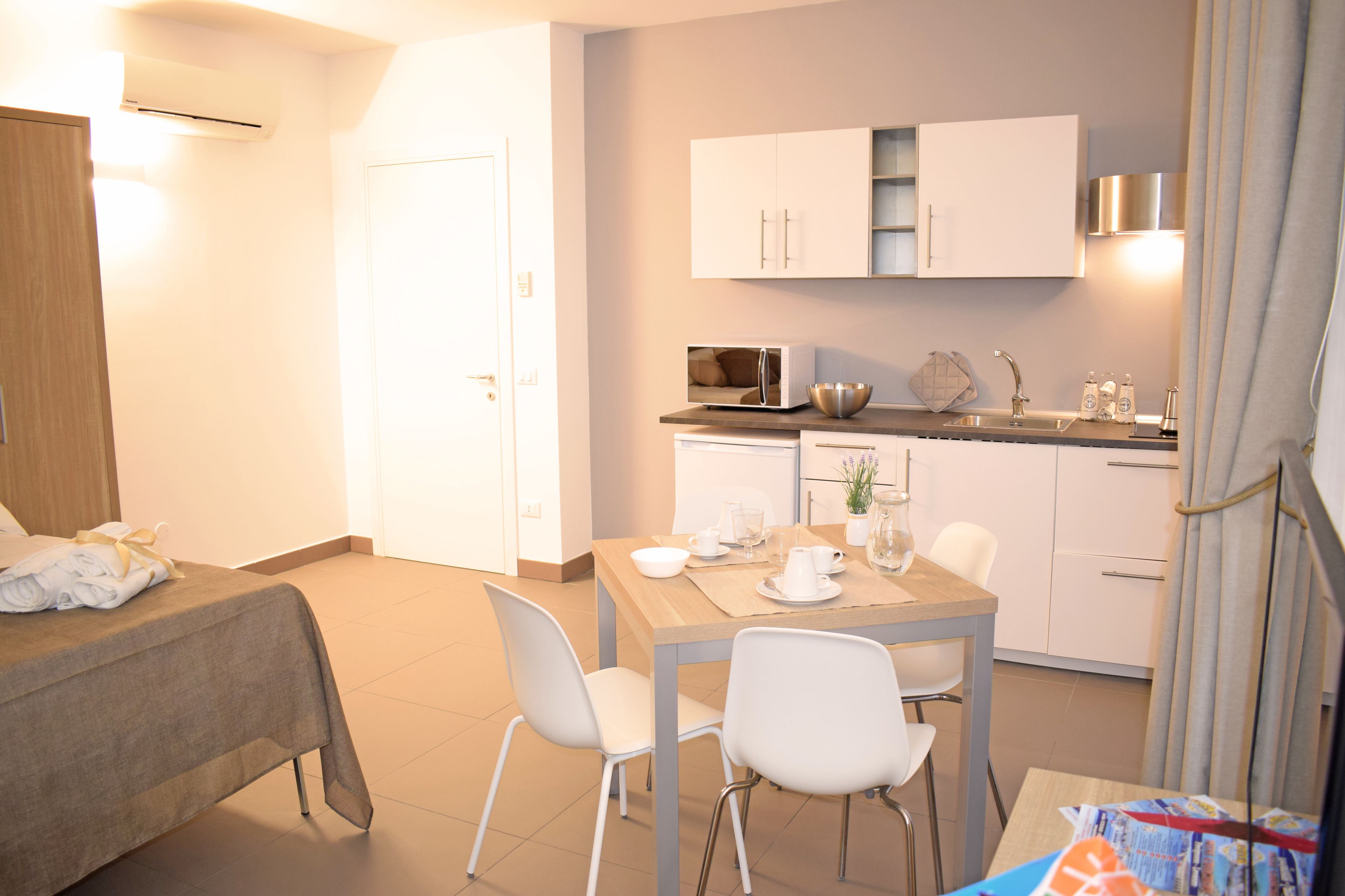 A hotel room with a bed, a dining table with chairs, a kitchen area with cabinets and appliances, and a bathroom with a shower curtain.
