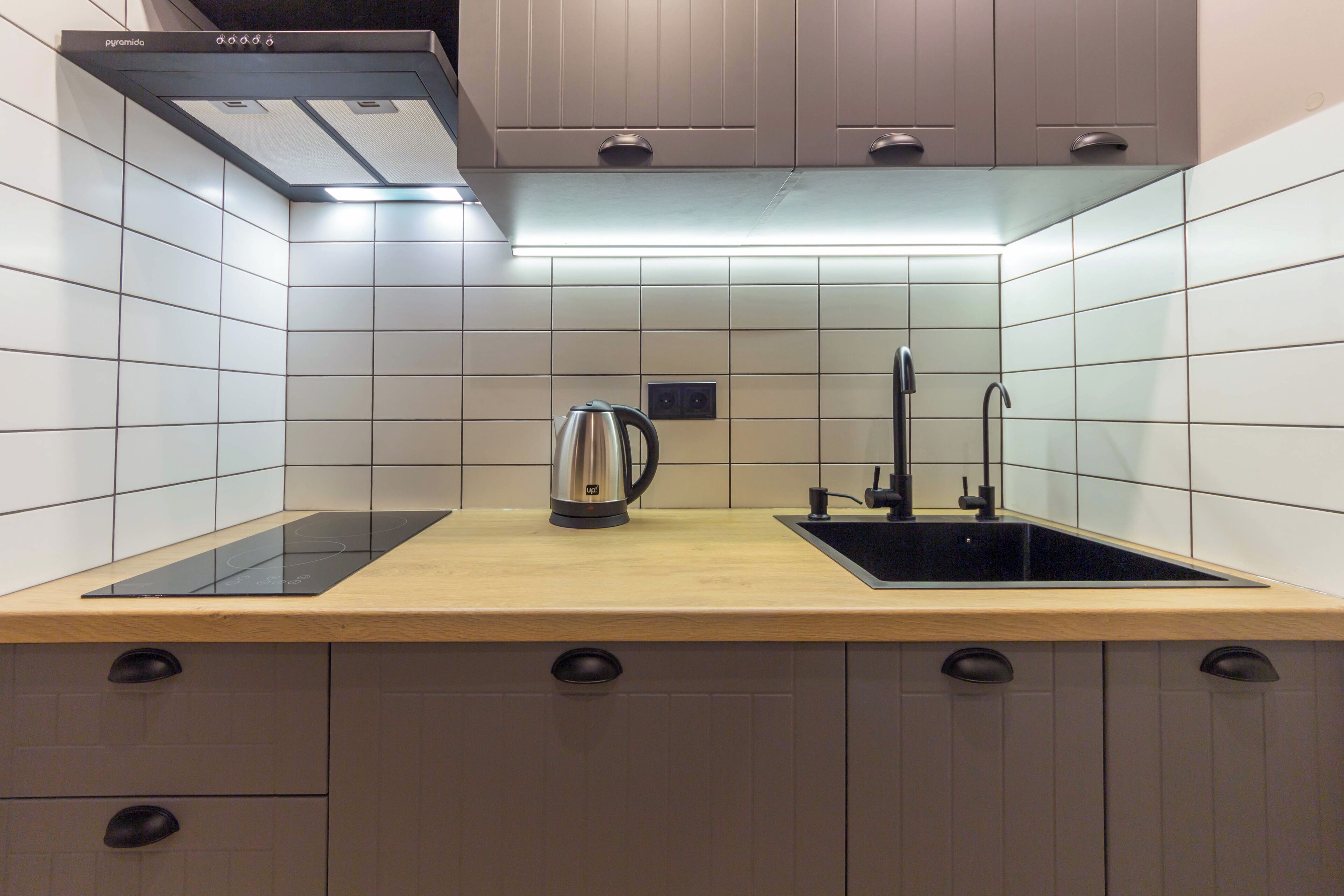 A modern kitchen with a wooden countertop, a built-in stove, a kettle, and a sink.