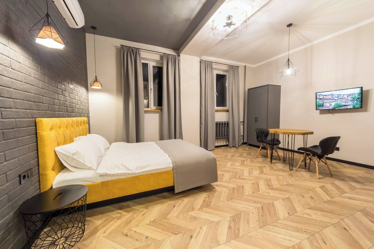 A modern hotel room with a bed, a small table, a chair, a TV, and a wardrobe.