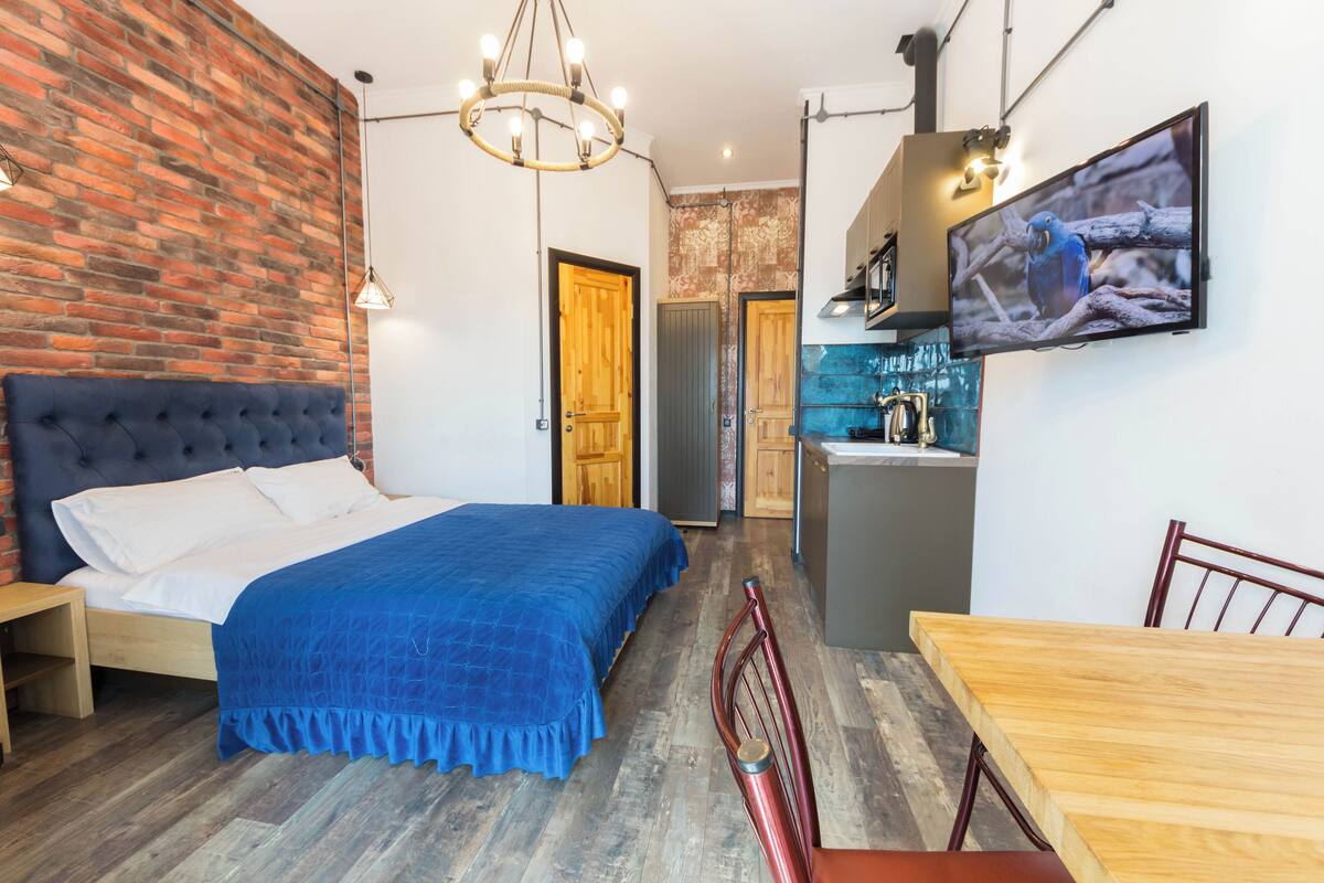 A bedroom with a large bed, a wooden headboard, a blue bedspread, a wooden dining table, and a red chair.