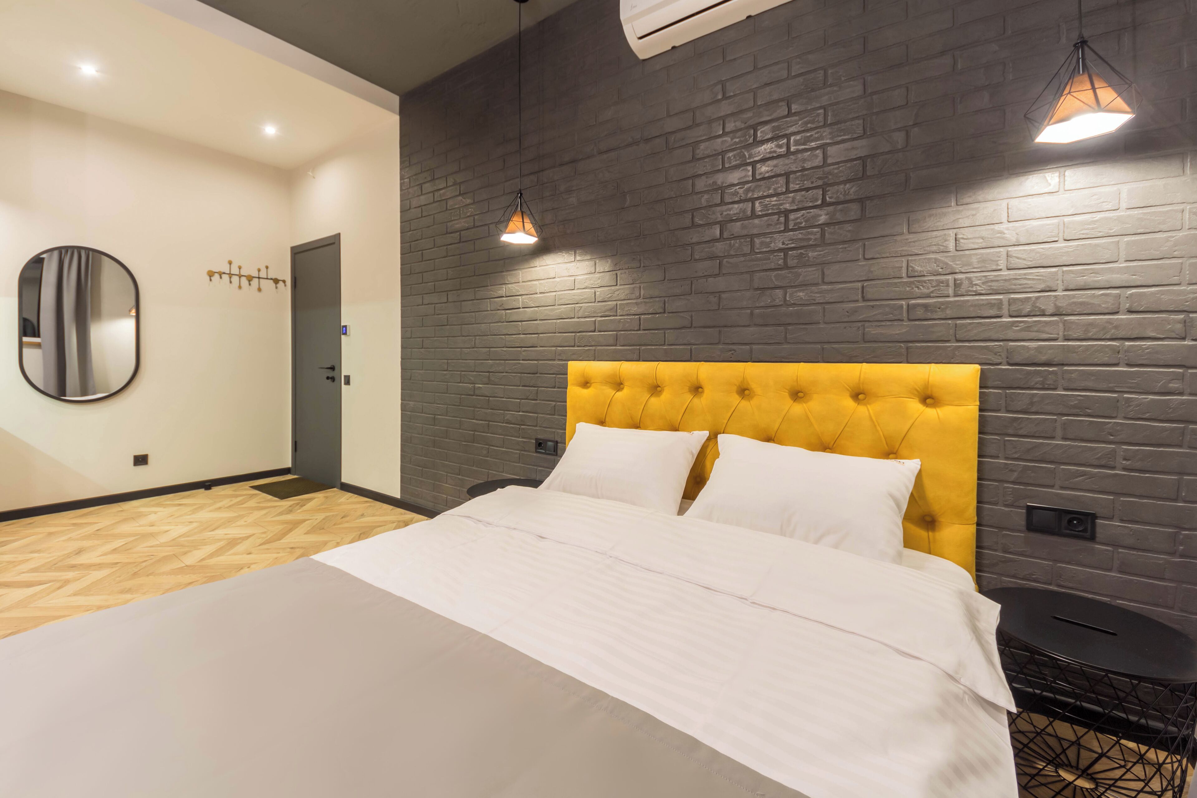 Een moderne slaapkamer met een groot bed, een geel, gestapeld hoofdeinde, een ronde spiegel en een metselwerk muur.