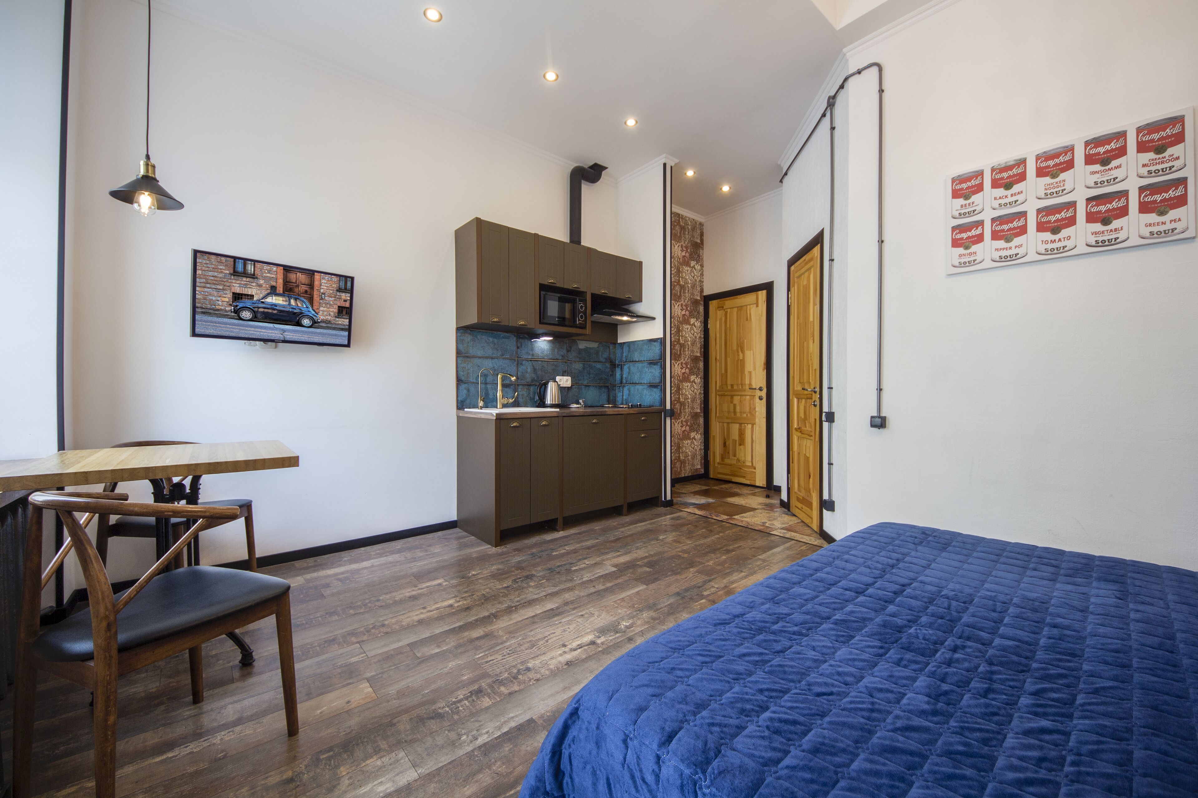 Una habitación pequeña con cama, una mesa de comedor con sillas, una kitchenette y una puerta que da a otra habitación.