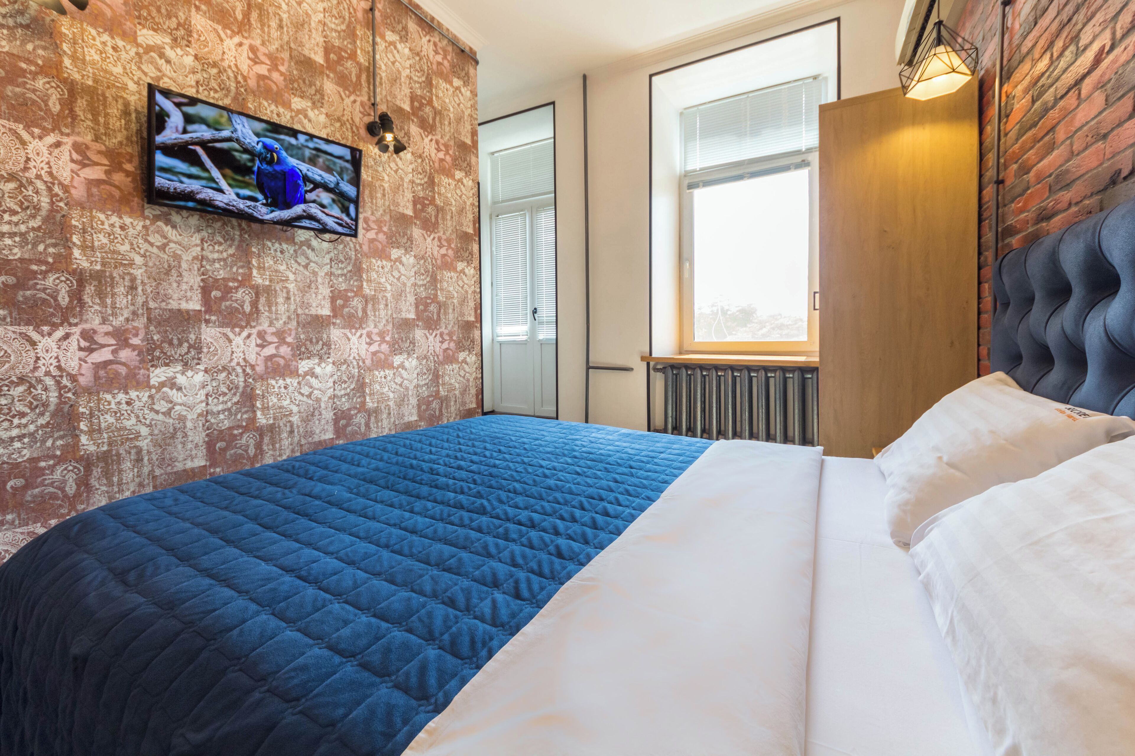 A modern hotel room with a large bed, a television mounted on the wall, and a window with blinds.