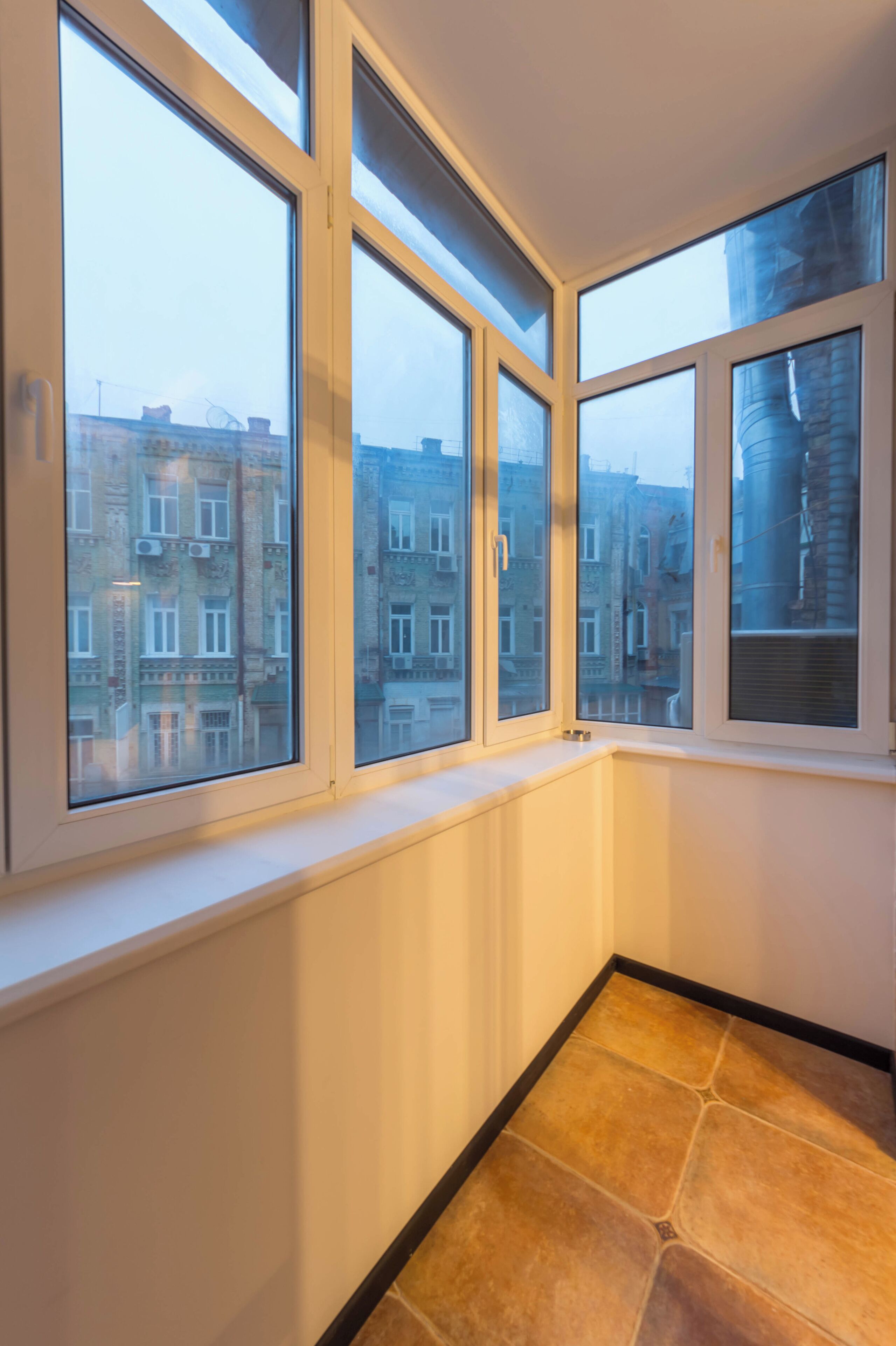 Habitación de esquina con ventanas amplias, un radiador y suelo de baldosas.