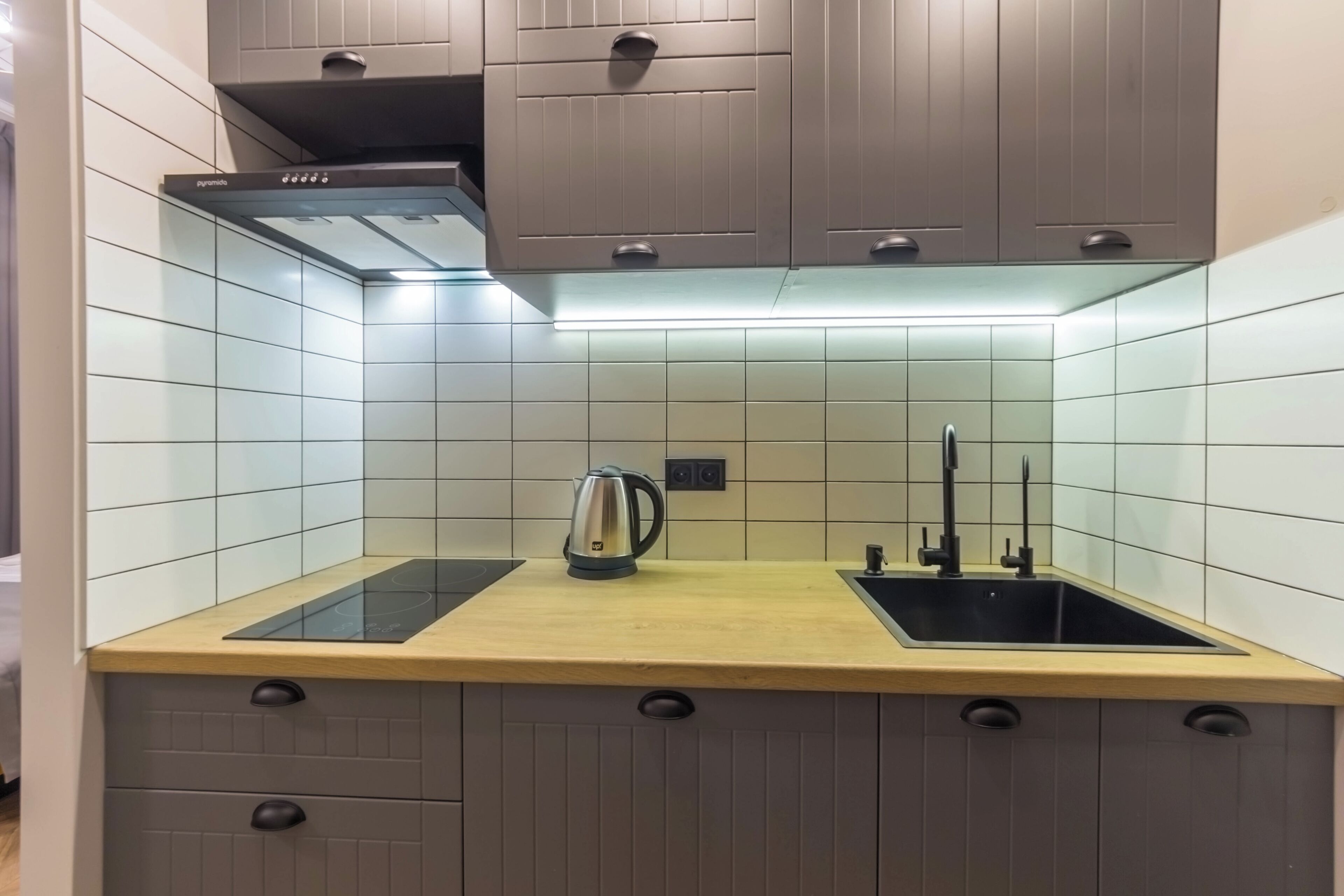 Una cocina moderna con encimera de madera, estufa integrada, hervidor y pileta.