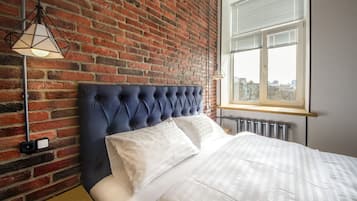 Camera da letto con parete in mattoni, una testiera imbottita, un letto con lenzuola bianche e una lampada a sospensione.