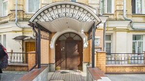 Entrada de um edifício com porta de madeira, grade de metal e parede de tijolos.