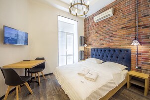 Een hotelkamer met een bakstenen muur, een groot bed met een gestuikt hoofdbord, een houten bureau met twee stoelen, en een televisie aan de muur.
