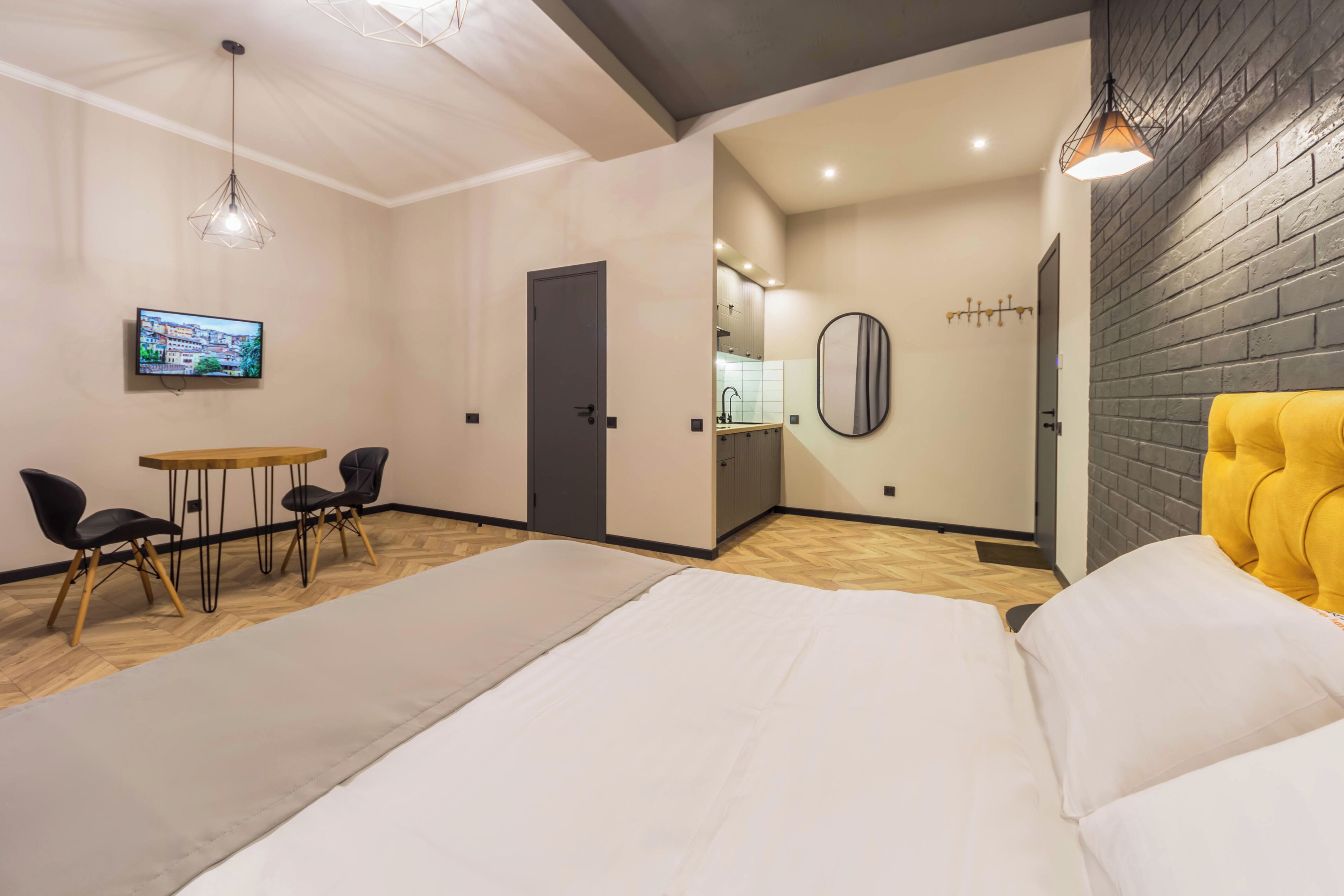 Une chambre d’hôtel comprenant un lit, un coin repas avec des chaises, un téléviseur et un coin cuisine visible à travers une porte ouverte.