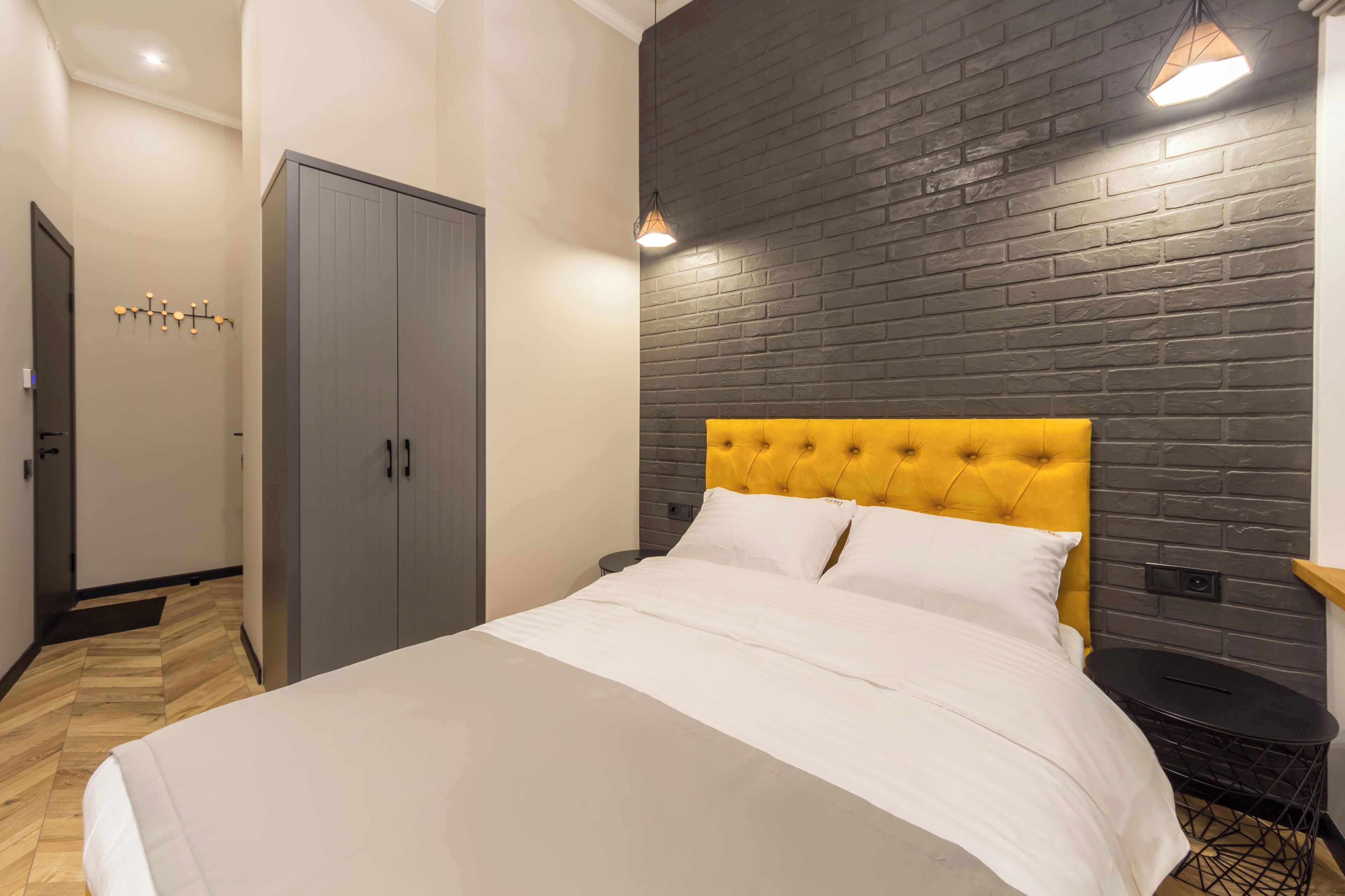 A bedroom with a bed, a wardrobe, a nightstand, and a brick-patterned wall.