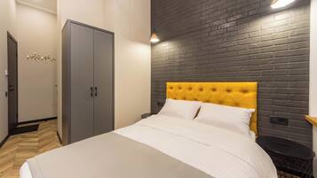 A bedroom with a bed, a wardrobe, a nightstand, and a brick-patterned wall.