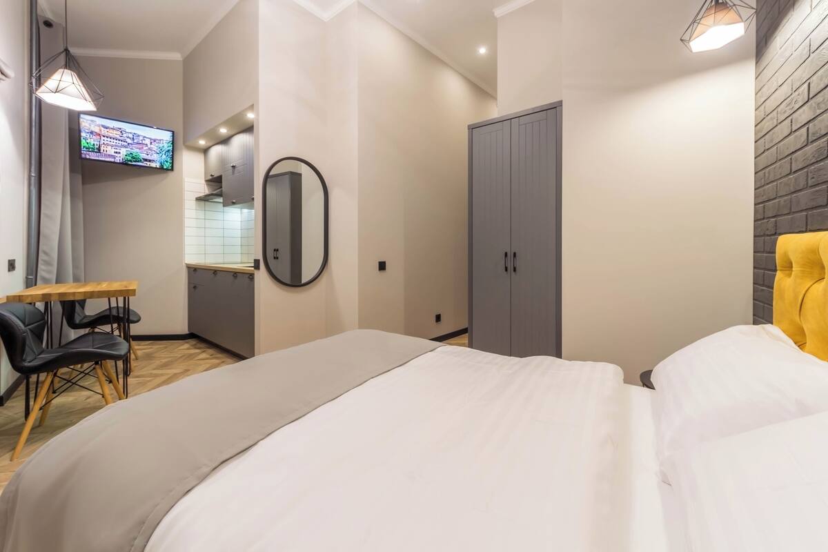 A modern bedroom with a large bed, a desk, a chair, a wardrobe, and a television on the wall.