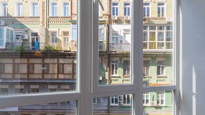 Quarto com amplas janelas que dão para um estacionamento e edifícios altos.