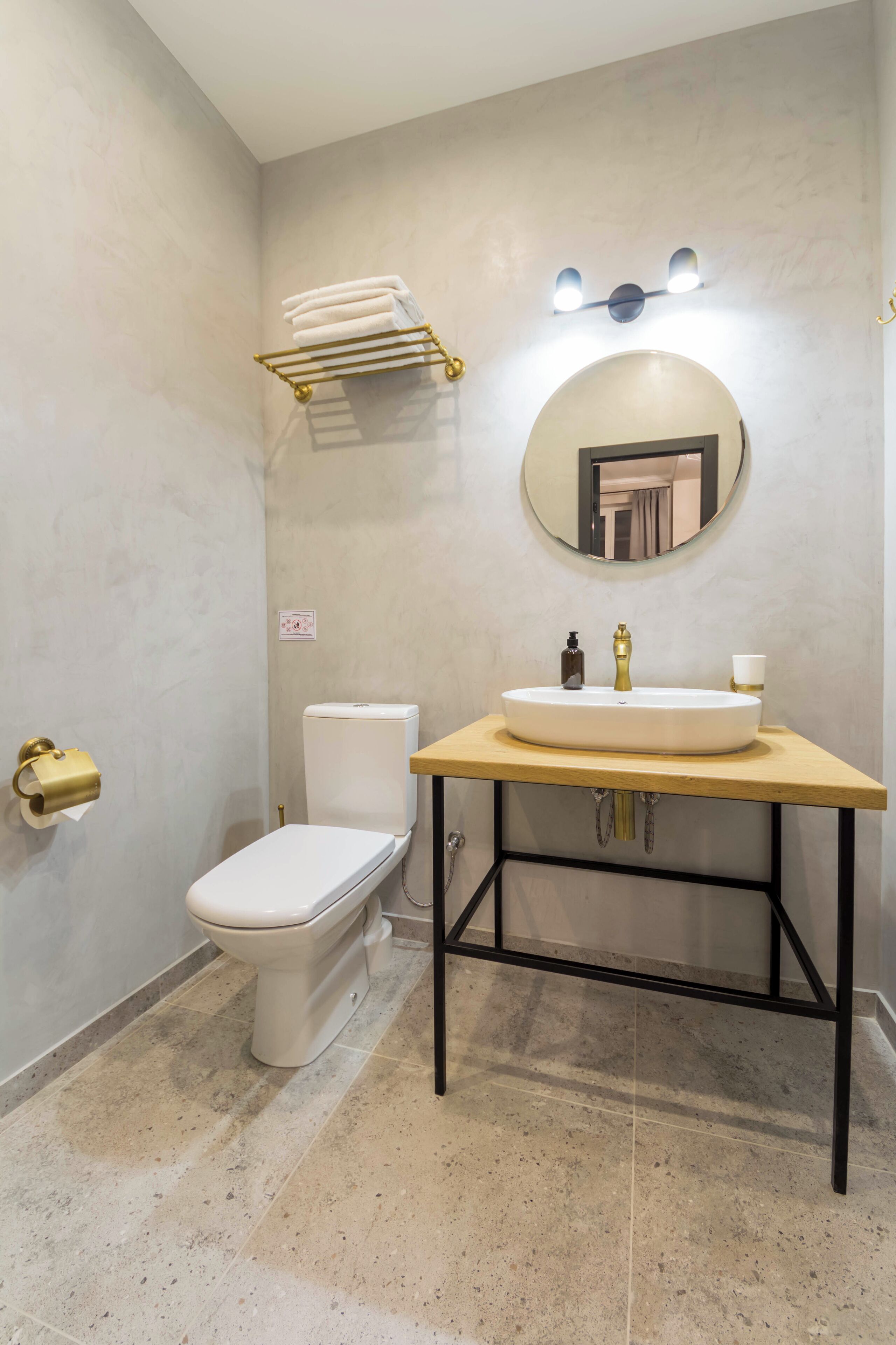 Ein Badezimmer mit einer weißen Toilette, einem runden Spiegel, einem Waschbecken mit goldener Armatur und einem Handtuchhalter.