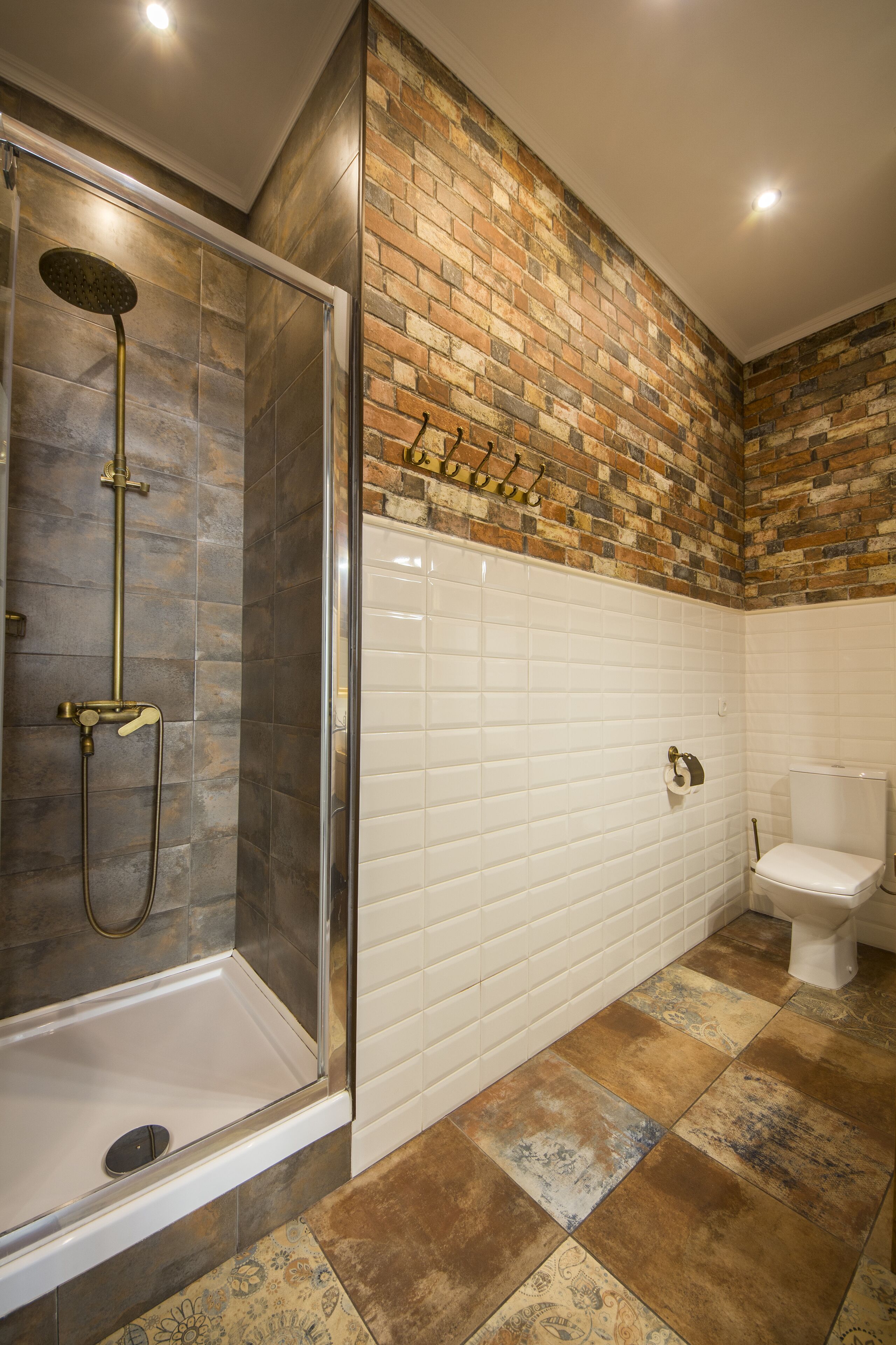 A bathroom with a glass-enclosed shower, white tiled walls, and a brick accent wall.