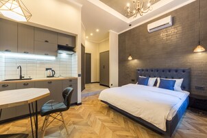 Een moderne hotelkamer met een keukenhoek, een eettafel en een groot bed met een gestapeld hoofdeinde.