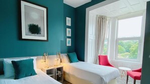 A hotel room with two beds, a desk, a chair, and a window with a view of greenery. - Rose Lodge Guest House (Cork)