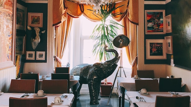 A dining area with a chandelier, a large elephant sculpture, and framed artwork on the walls. - Rose Lodge Guest House (Cork)