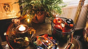 A table with a candle, a plant, a basket of apples, and a bowl of assorted snacks. - Rose Lodge Guest House (Cork)