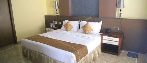 A hotel room with a large bed, a nightstand, a lamp, and a wall-mounted TV.