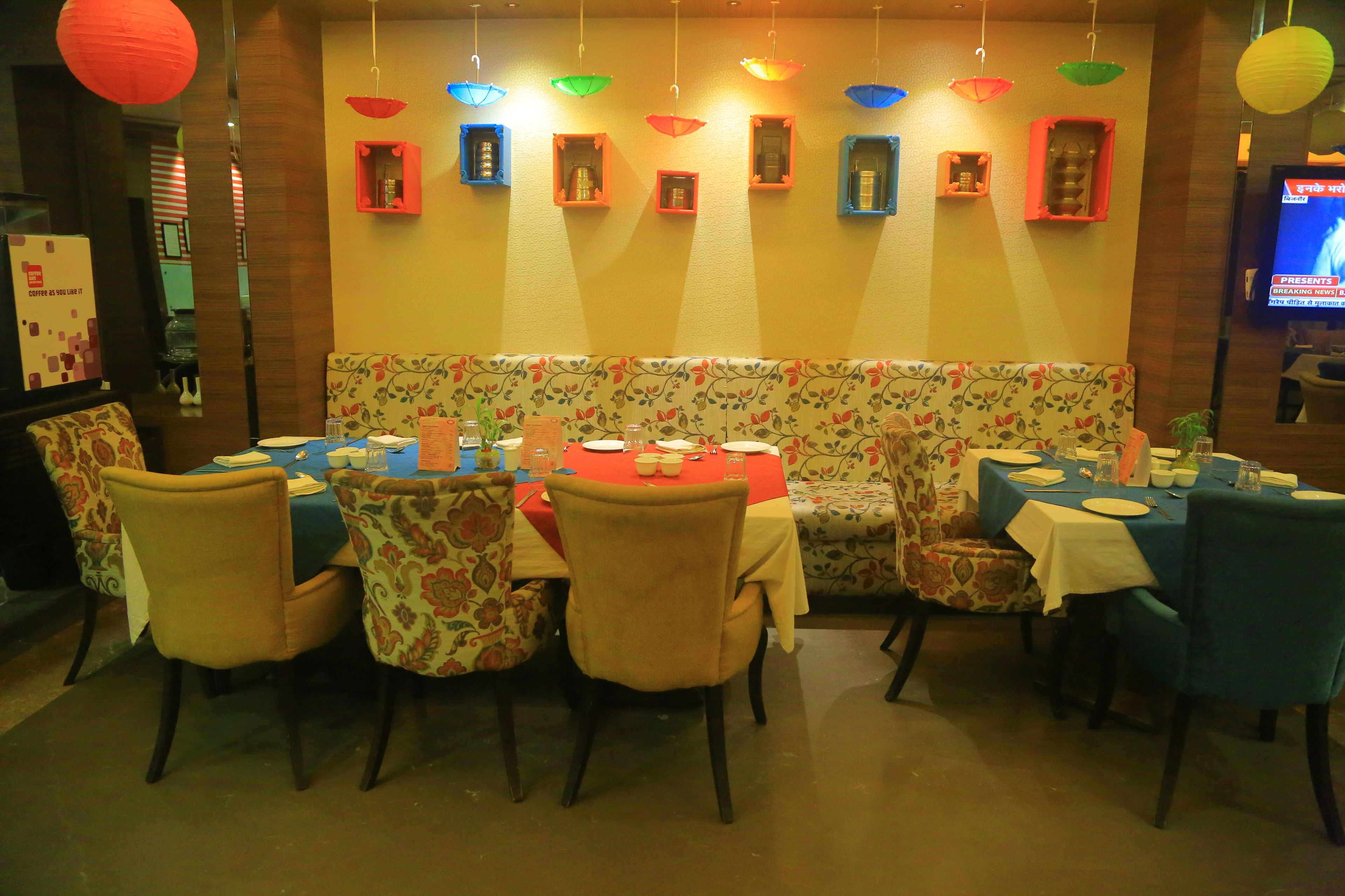 A restaurant with a booth seating area, tables with blue tablecloths, and colorful hanging lights.