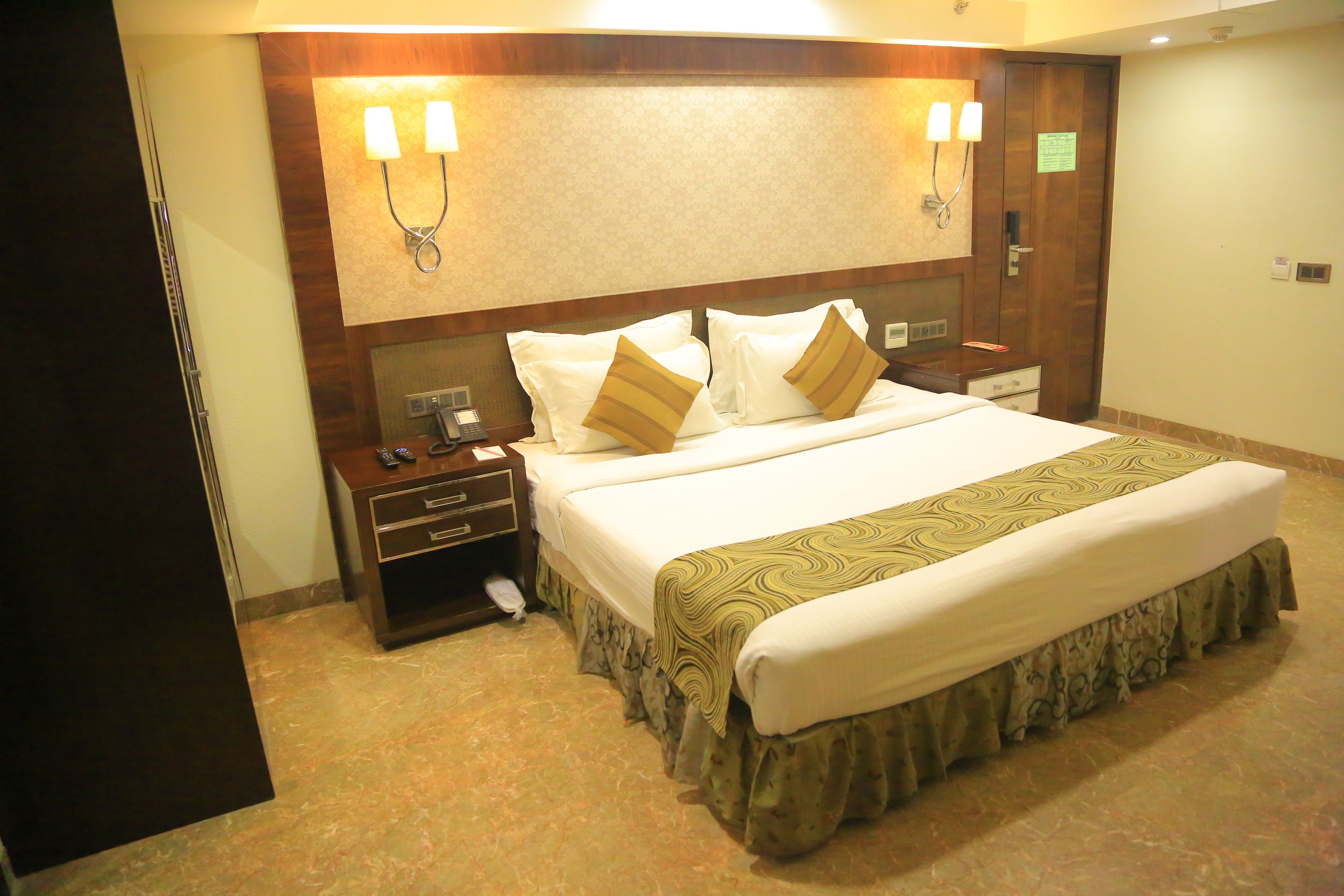 Una habitación de hotel con una cama grande, mesitas de noche, un teléfono y lámparas de pared.