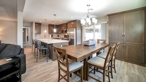 Cocina moderna con una isla central, mesa de comedor de madera y sillas. Cuenta con electrodomésticos de acero inoxidable, luces colgantes y armarios de madera.