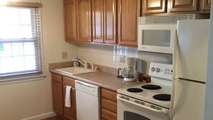 A kitchen with wooden cabinets, a white countertop, a built-in microwave, a stove, and a dishwasher.