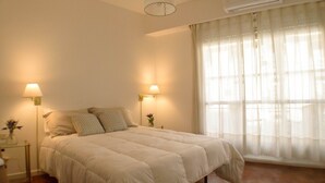 Ein Schlafzimmer mit einem Bett, zwei Nachttischlampen, einer Klimaanlage und leicht transparenten Vorhängen.