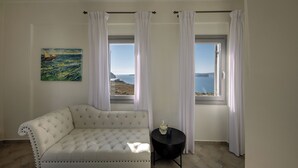 Una stanza con un divano bianco, un tavolino rotondo con un boccale e un bicchiere, e un quadro raffigurante una barca a vela appeso al muro.