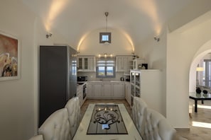A modern kitchen with white cabinets, a dining area with a glass-top table, and a view through the window.
