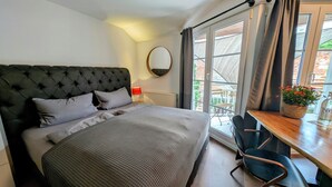 Une chambre avec un grand lit, un miroir rond, une table avec des chaises et une vue sur l’extérieur.