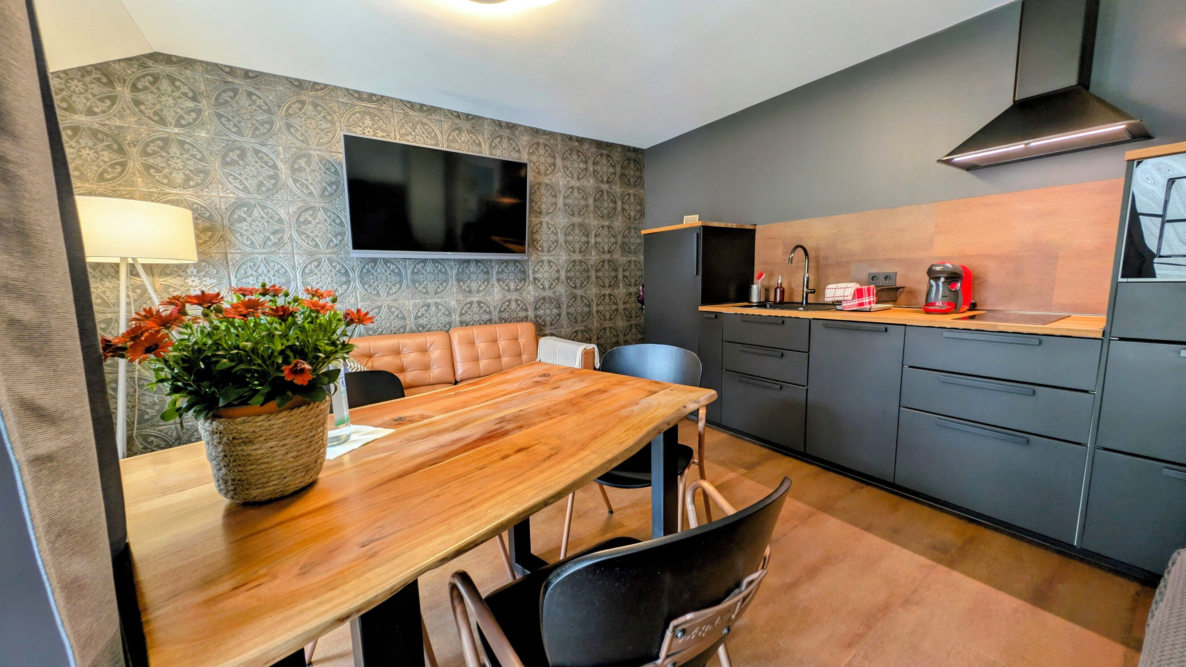 A modern kitchen with a wooden dining table, a built-in oven, and a black range hood.