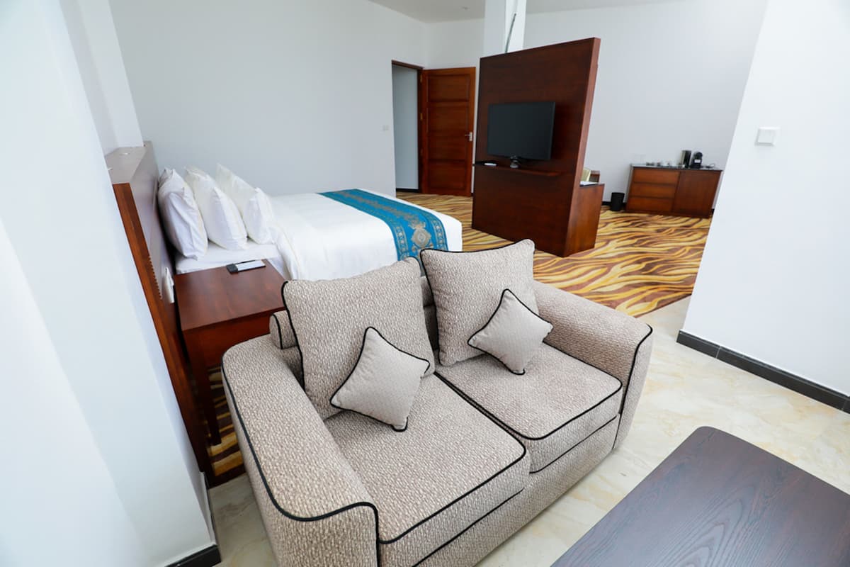 A hotel room with a sofa, a bed with a TV, a wooden wardrobe, and a patterned carpet.