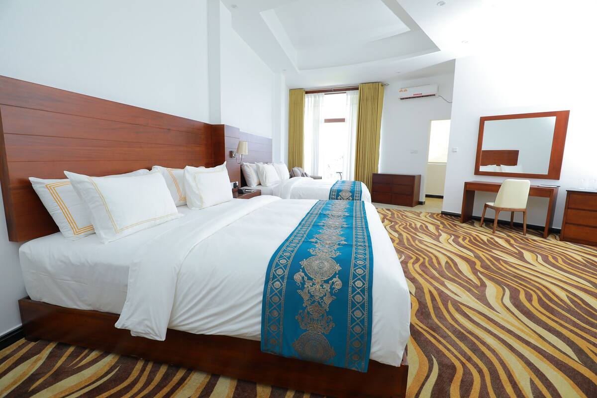 A hotel room with a large bed, a desk, a chair, and a mirror.