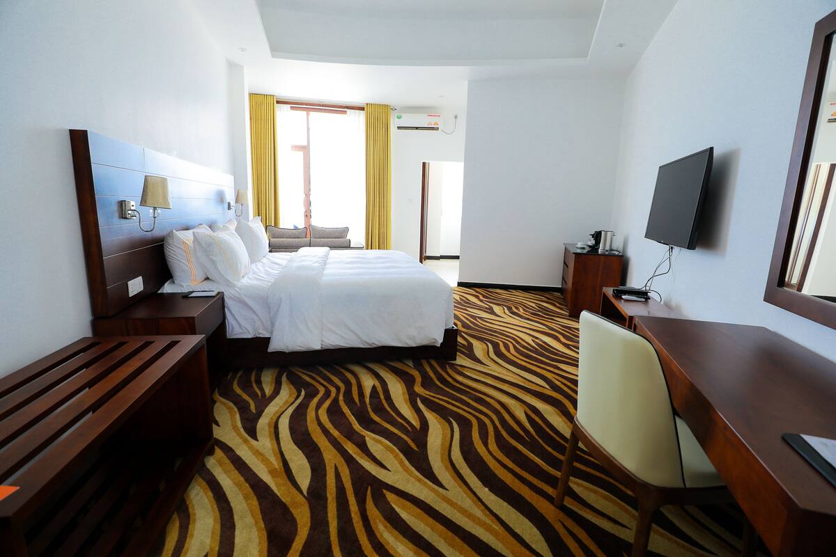 A hotel room with a bed, a desk, a chair, a television, and a patterned carpet.