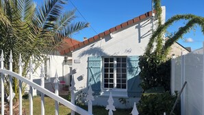Une maison blanche avec un toit rouge, une fenêtre bleue et une clôture blanche.