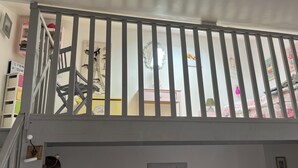 Une pièce avec une rambarde blanche, un escalier, une horloge murale et un tableau représentant des fleurs.