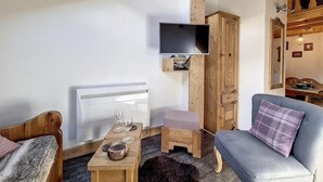A cozy living room with a sofa, a small table with glasses, a TV mounted on a wooden wall, and a radiator. - 50m from resort center, 3rd floor, tv, ski locker, 22m², Saint Martin de Belleville (Saint-Martin-de-Belleville)