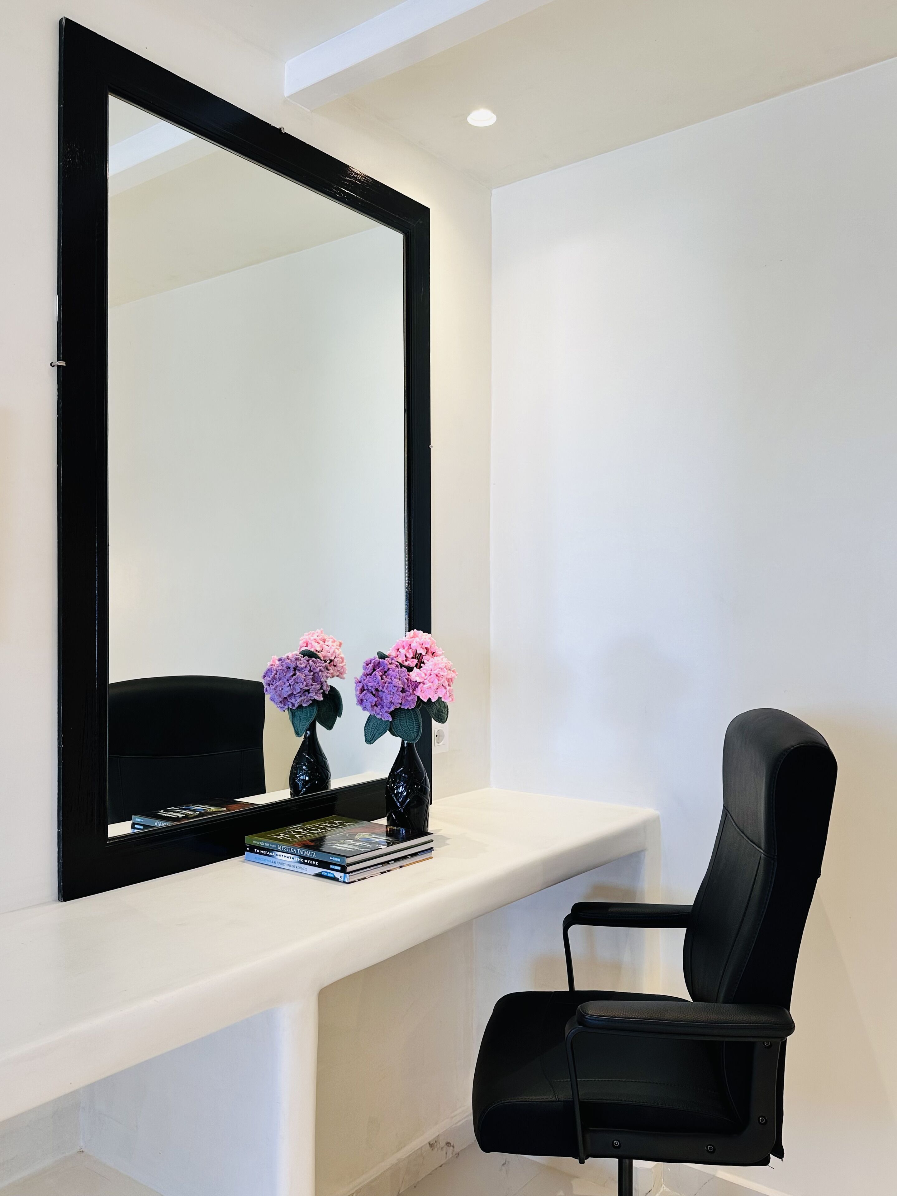 A modern room with a large mirror, a black office chair, a white console table, and two vases with flowers.