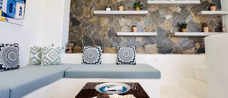 A modern living room with a stone wall, white furniture, and decorative pillows.