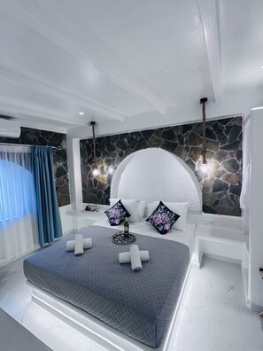 A modern bedroom with a large bed, stone wall, and a stone fireplace. - Arlene Suites (Santorini)