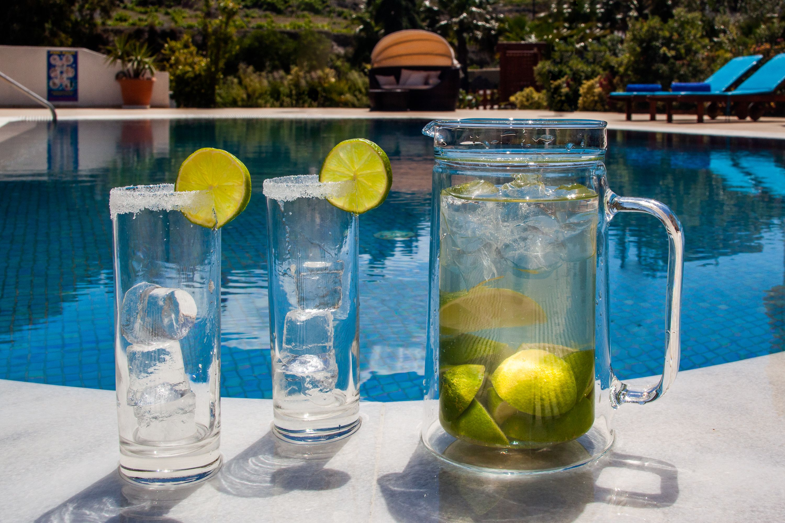 Three glasses of iced beverages with lime slices by a poolside.