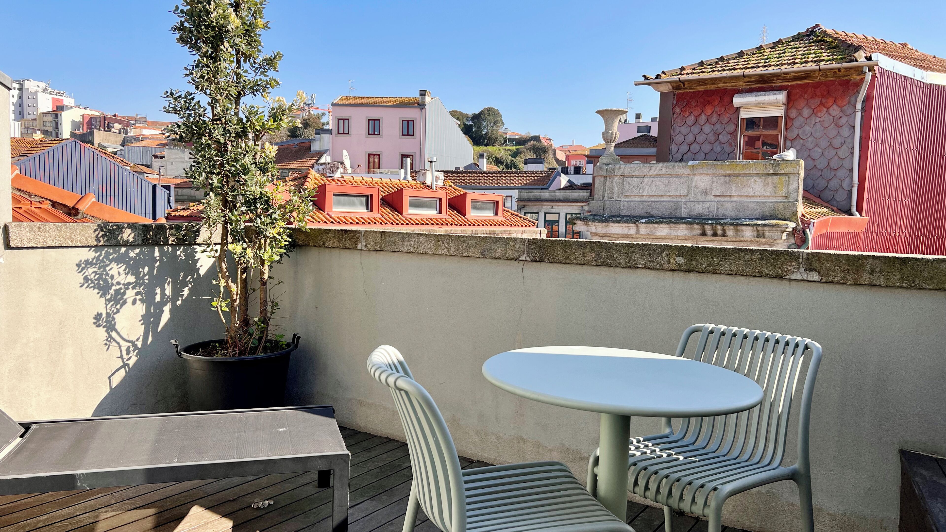 A rooftop terrace with a table and chairs, a potted plant, and a view of the cityscape.