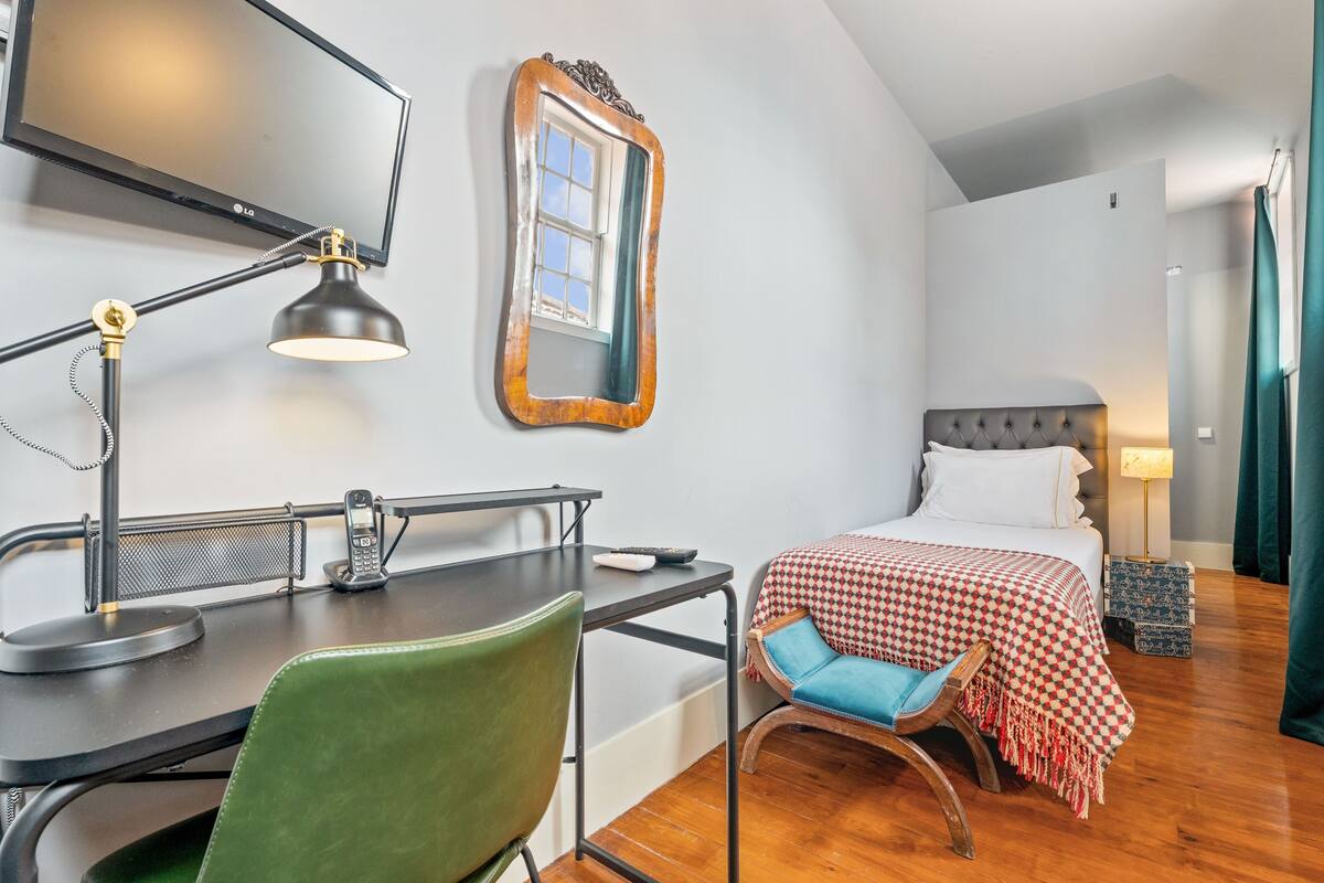 A compact hotel room with a desk, chair, bed, and a mirror on the wall.