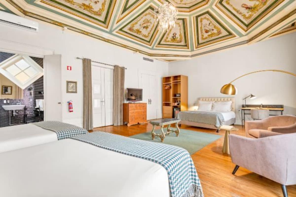 A hotel room with a large bed, a smaller bed, a desk, a chair, a wardrobe, and a kitchenette.